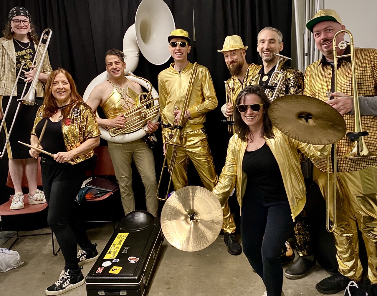 People posing for the camera with brass instruments and percussion dressed in metallic gold clothes.